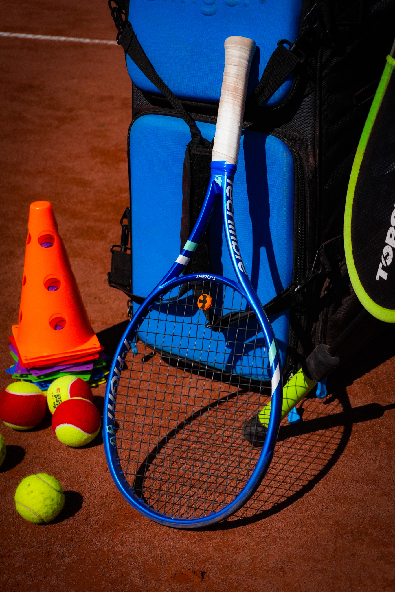 Tennisschläger, Trainingsbälle und Markierungshütchen auf einem Sandplatz