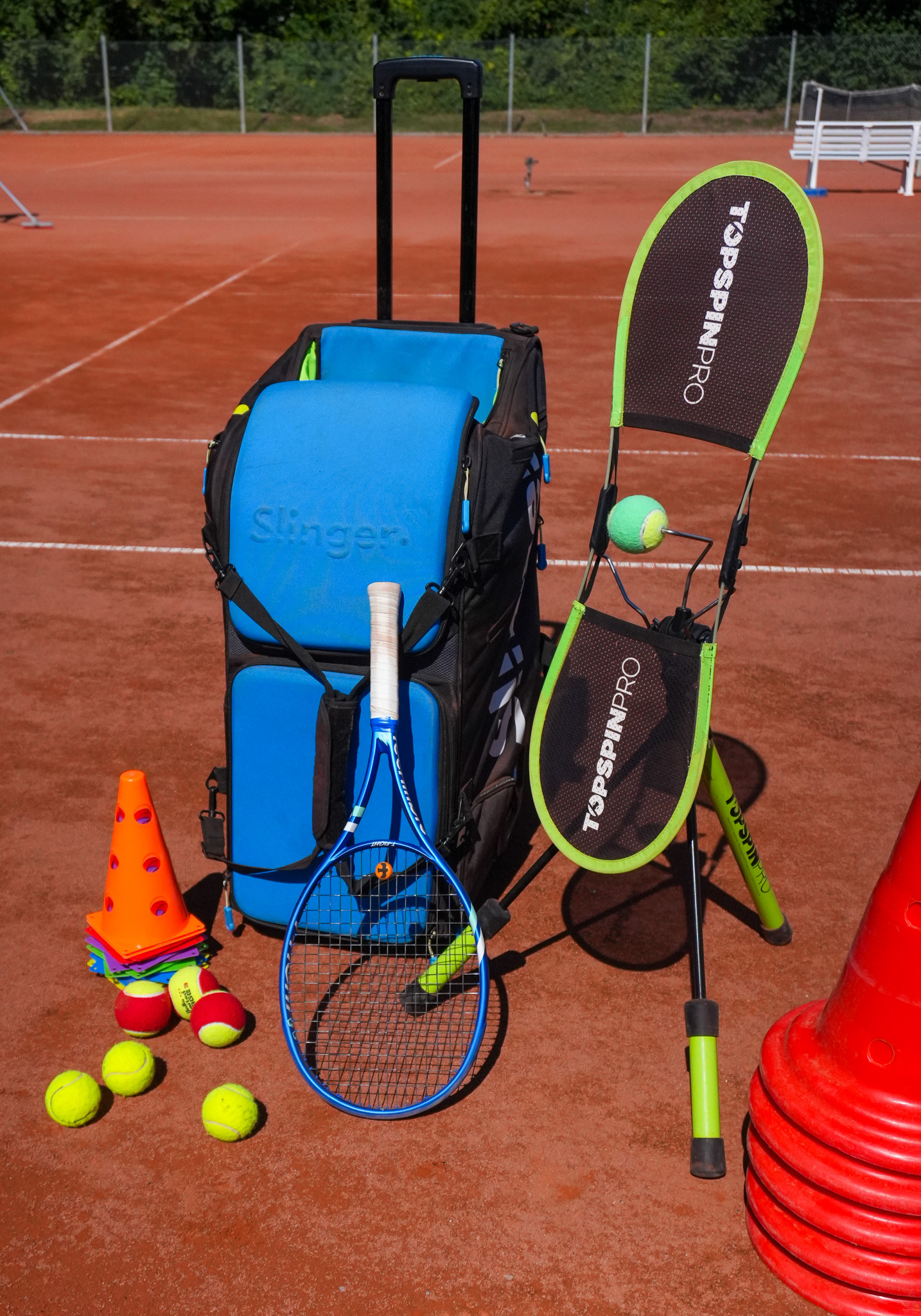 Trainingsausrüstung mit Tennisschläger, Bällen und Zielhilfen auf einem Sandplatz